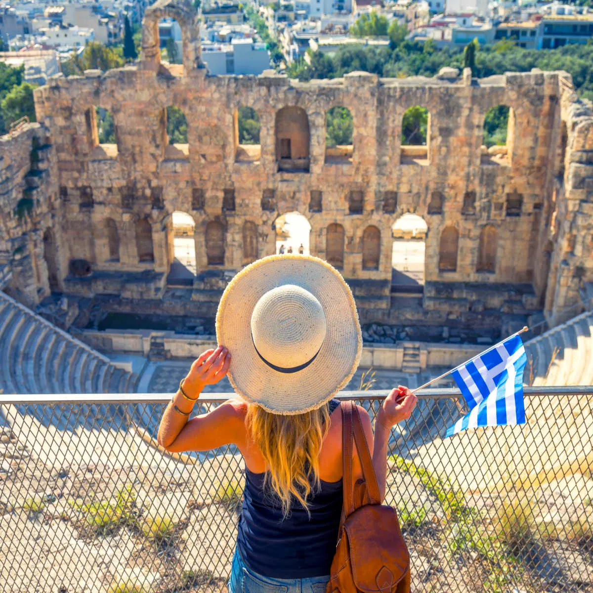 American Airlines Launching 5 New Routes To Popular International Destinations Tourist holding Greek flag at Theatre of Herodion - Athens, Greece