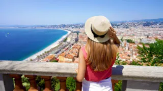 French Riviera. Back view of beautiful young woman holding hat enjoying the cityscape of Nice, France.