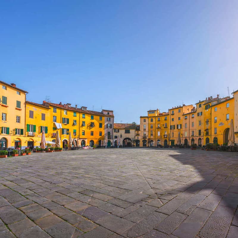 Main Medieval Square Surrounded By Pastel Colored Buildings In Lucca, Italy