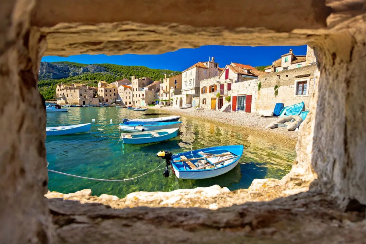 Scenic beach in Komiza waterfront view through stone window, Island of Vis, Croatia