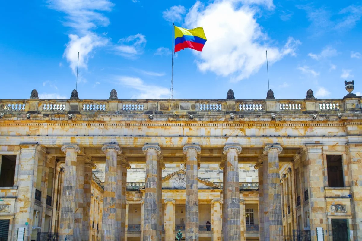 Travelers Can Now Explore Colombia By Train For First Time In Over 50 Years Colombia flag waving over historic building in Bogota