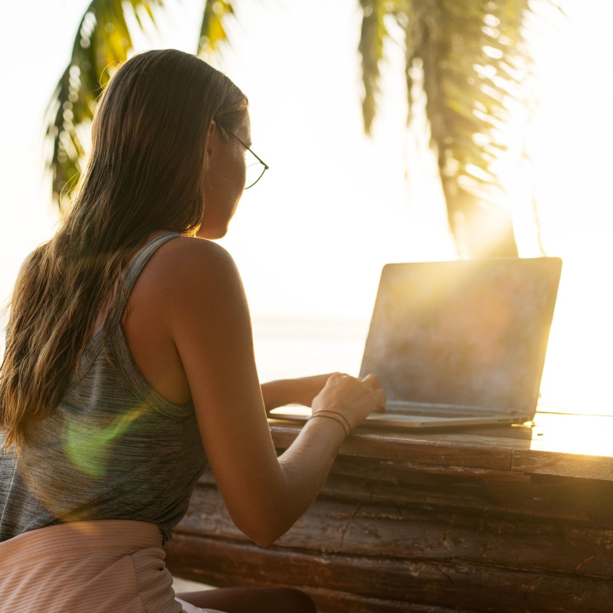 Digital nomad with laptop under palm tree