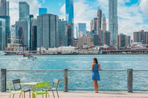 New York city Manhattan skyline seen from Brooklyn waterfront - woman enjoying view. American people walking enjoying view of Manhattan over the Hudson river from the Brooklyn side. NYC cityscape
