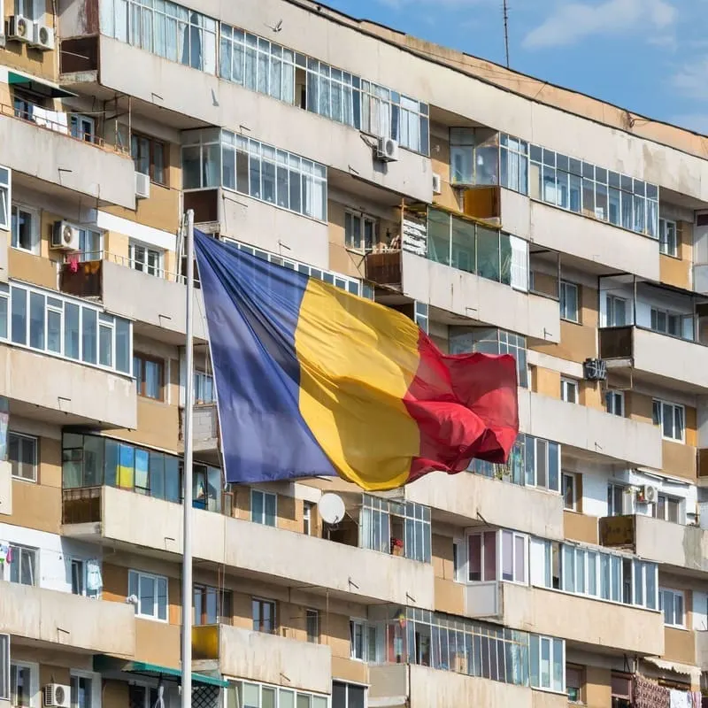 Romanian Flag Flying Against A Brutalist Apartment Block From The Communist Era, Bucharest, Romania