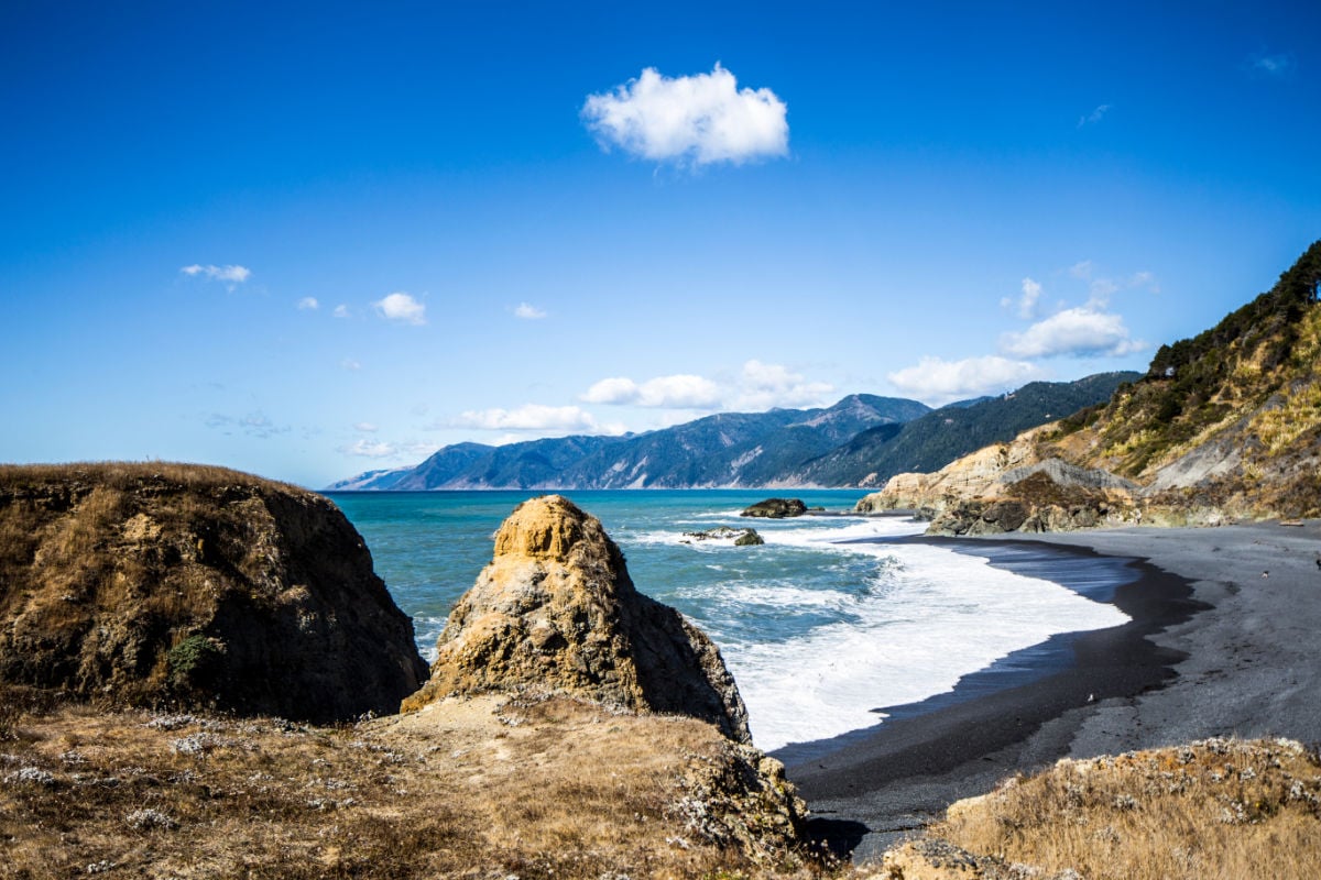View of the famous black sand at Black Sands Beach, Whitethorn, California near Shelter Cove. Amazing black sand beach with view mountains and rock structures.