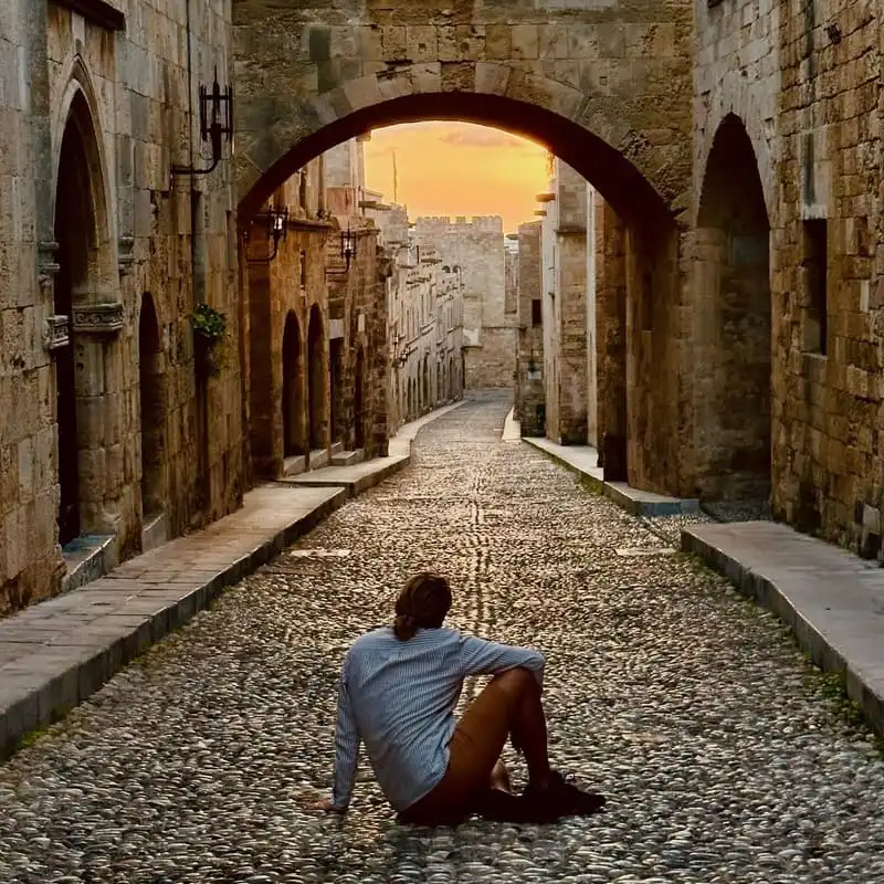 A Tourist Sitting On The Cobblestones Of Street Of The Knights, Rhodes Town, Greece