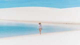 Woman next to a blue lagoon with white sand at Lençóis maranhenses national park, Brazil