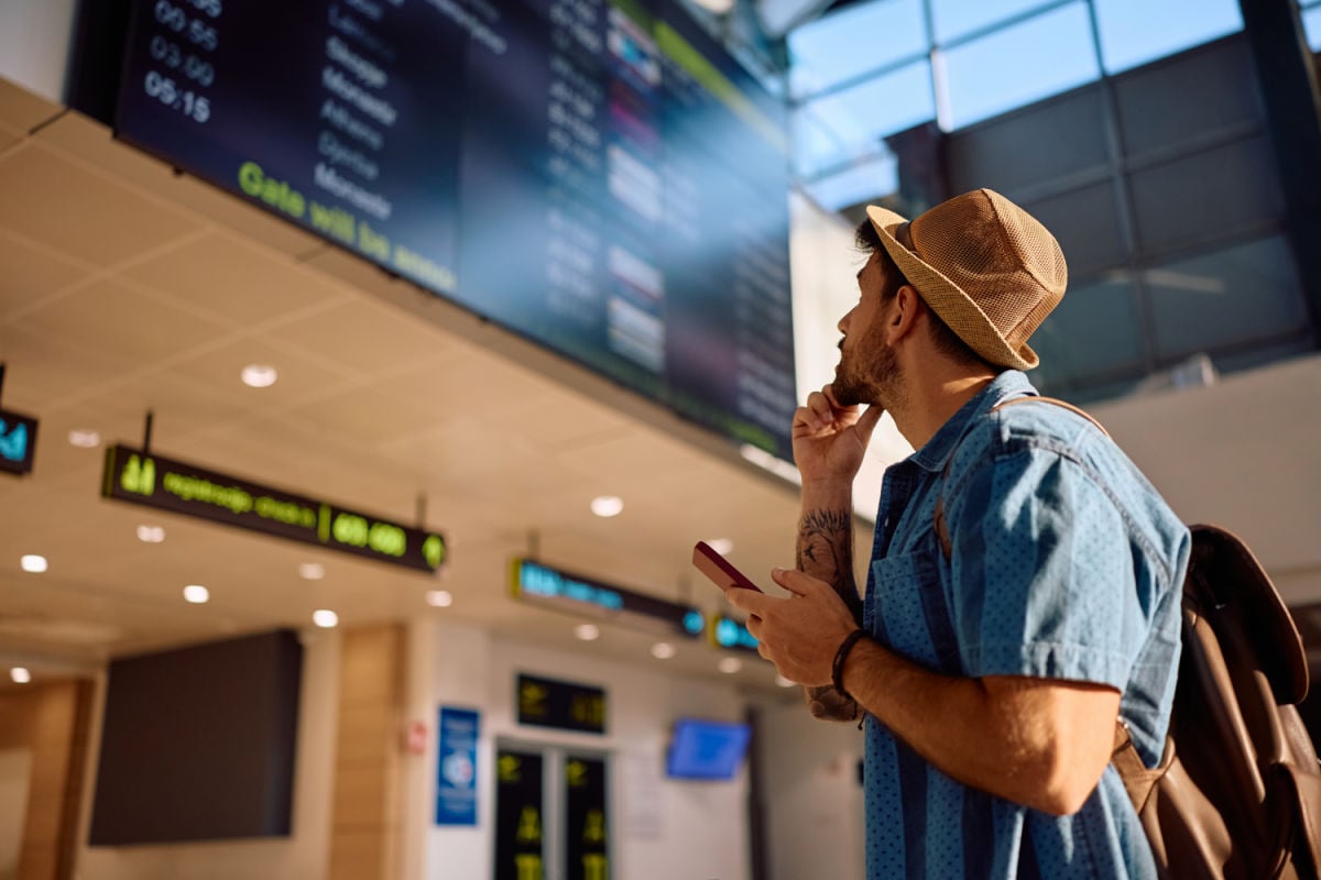 Male tourist in airport with phone looking at departures board