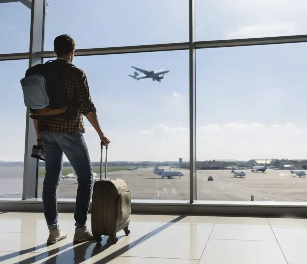 空港の窓際に立ち、離陸前の飛行機を眺めている男性。
