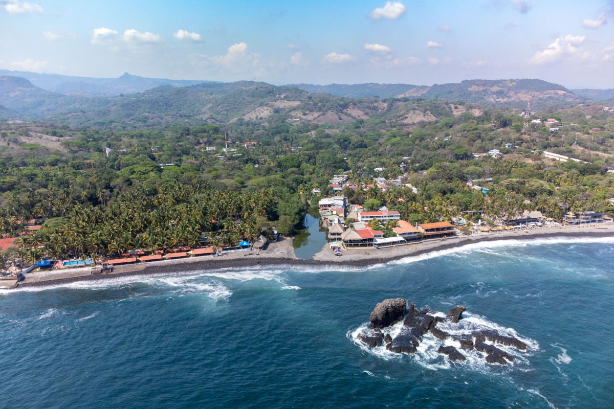 Aerial view of El Tunco beach with lush greenery and rock formations in El Salvador under a clear sky.