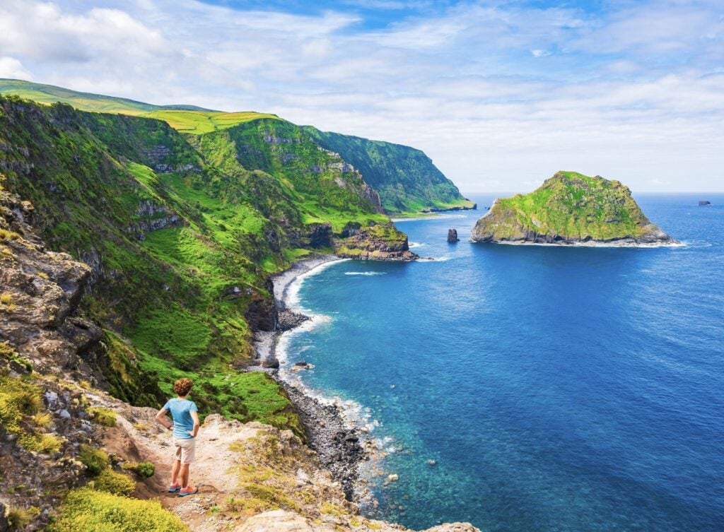 Young woman tourist looking at beautiful bay with beach and green cliffs at Baia de Alem, Flores island, Azores, Portuga