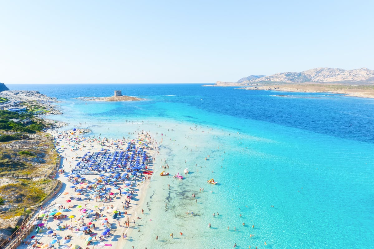 Beach La Pelosa, Sardinia, Italy. Summer vacation and rest. Beach, people and umbrellas. Top view from drone at the beach and azure sea. Background, wallpaper, postcards.