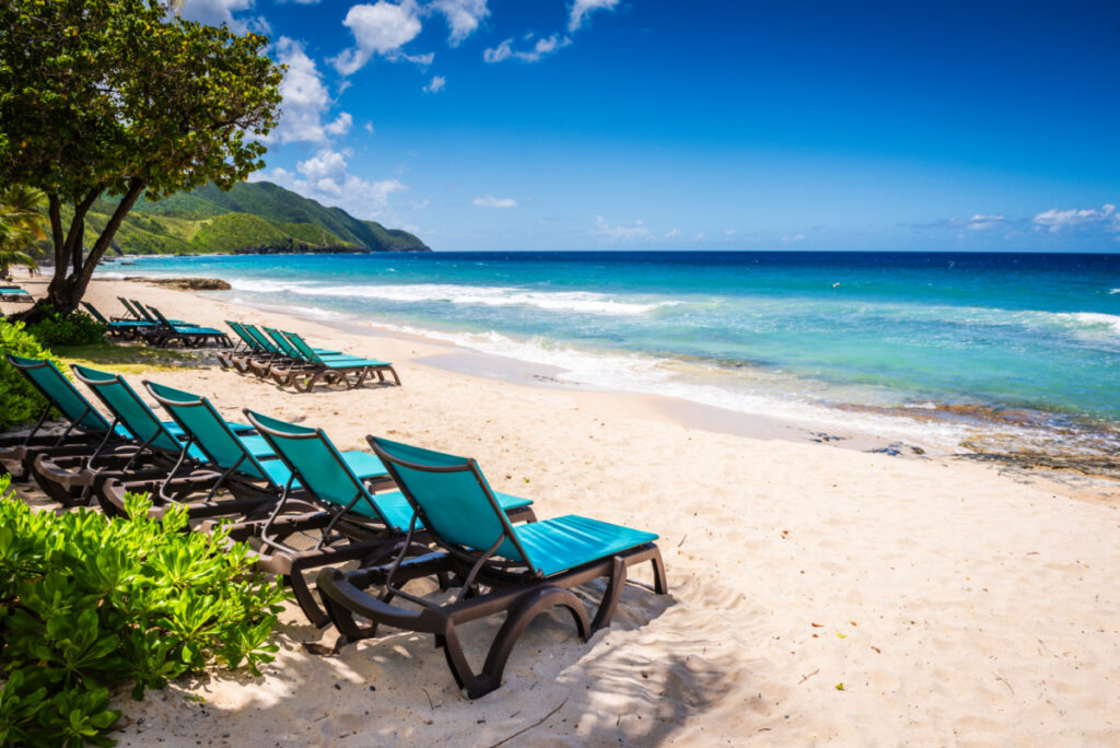 St. Croix, US Virgin Islands Two rows of teal fabric lounge chairs line white sand beach with a view of beautiful Caribbean Sea.