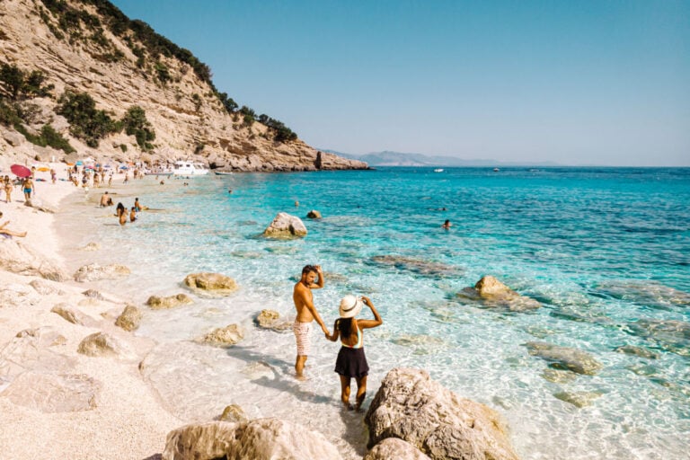 View from above, stunning aerial view of a beautiful beach full of beach umbrellas and people sunbathing and swimming on a turquoise water. Cala Gonone, Sardinia, Italy, Cala Mariolu