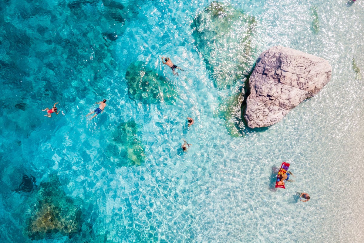 crystal-clear waters of Baunei, Sardinia, where people swim and relax on sun-kissed beaches.