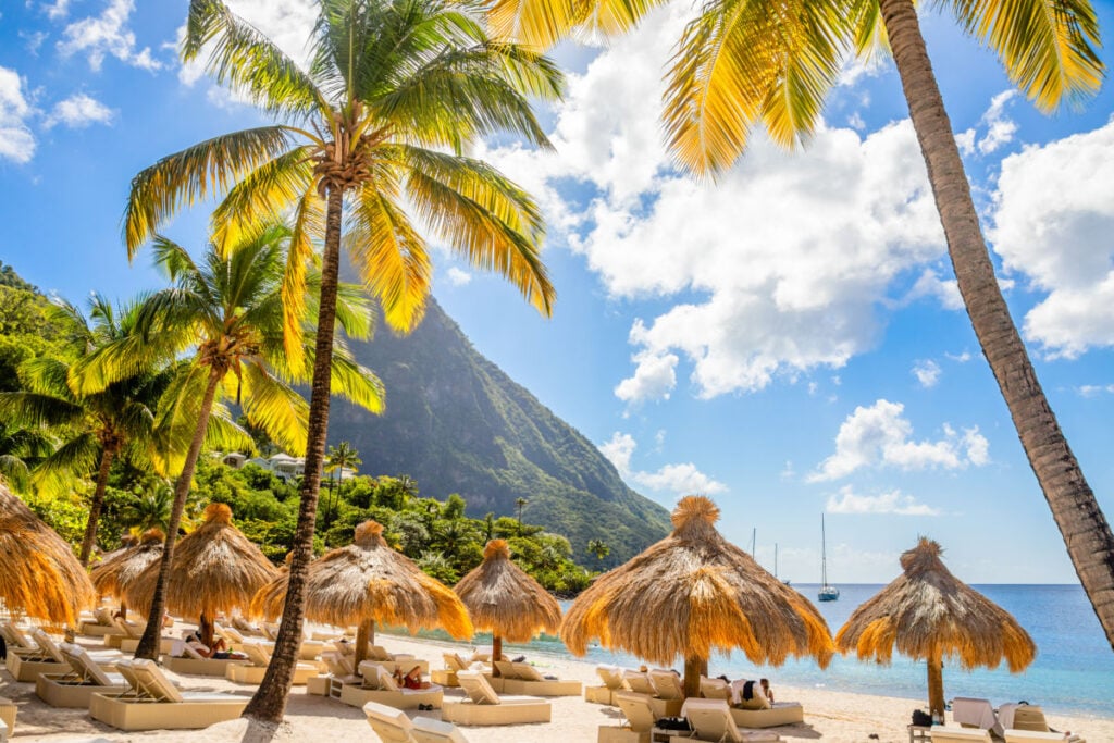 Caribbean beach with palms and straw umrellas on the shore with Gros Piton mountain in the background, Sugar beach, Saint Lucia