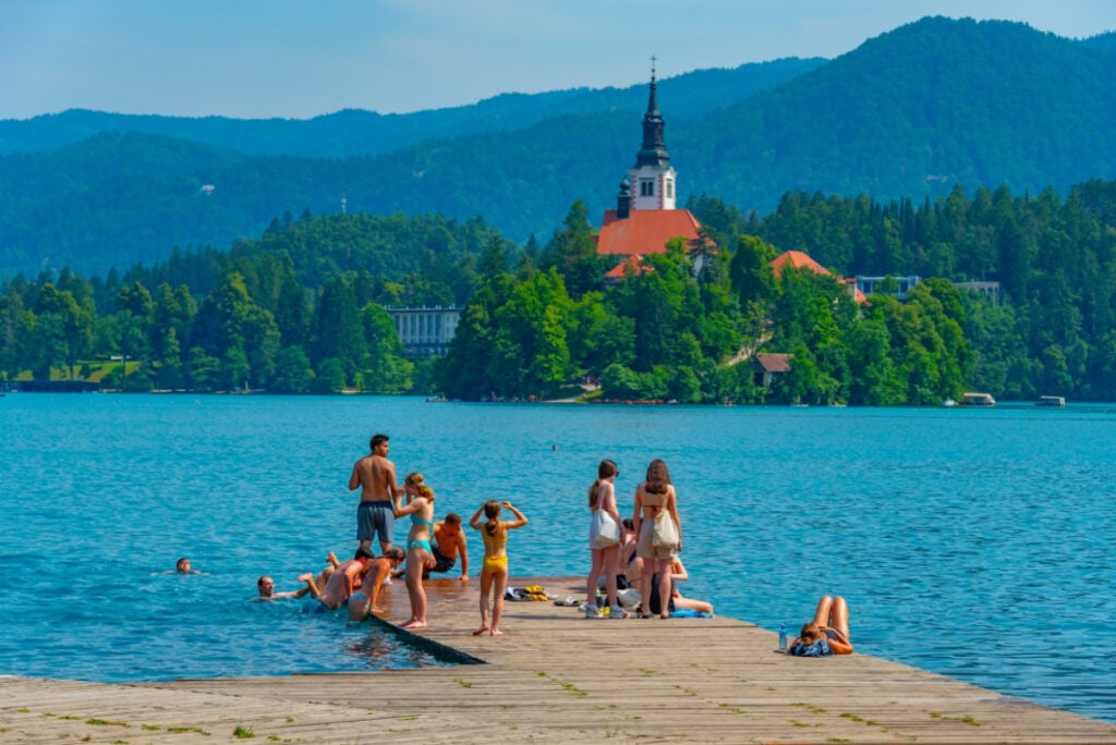 People are swimming in front of the Assumption of Maria church at lake Bled in Slovenia