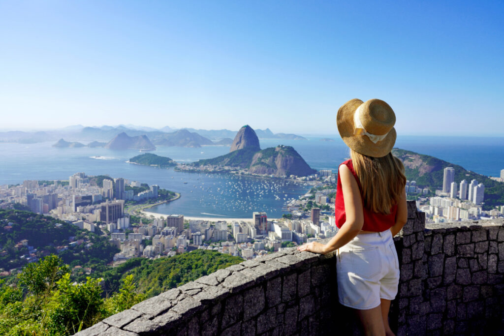Tourism in Rio de Janeiro. Back view of traveler girl enjoying sight of famous Guanabara Bay with Sugarloaf Mountain in Rio de Janeiro, UNESCO World Heritage, Brazil.