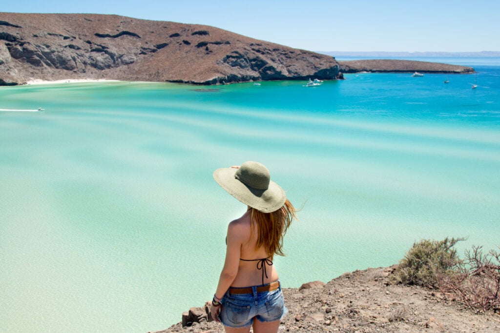 Young woman with a beach hat admiring the beautiful view of the Balandra Beach near La Paz from the top of the cliff.