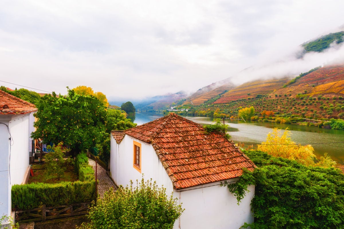 Autumn landscape of Douro river valley, Portugal. Traditional portugal architecture with red tile roof. Clouds over the mountains at foggy morning