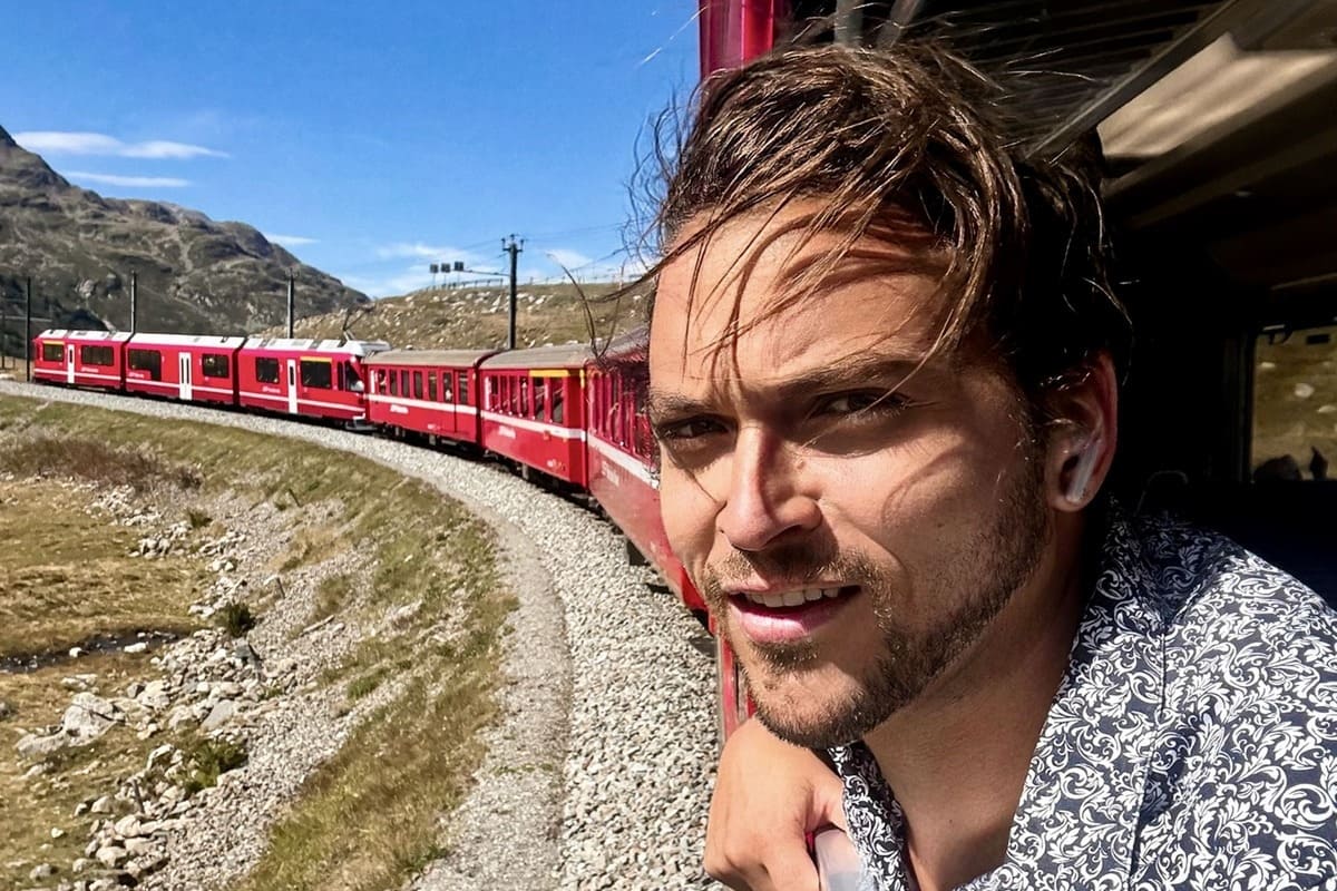 Male Traveler Smiling As He Rides The Red Regional Train From St Moritz Switzerland To Tirano Italy