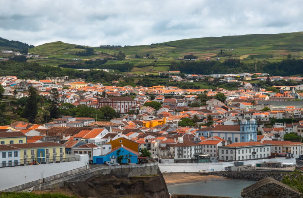 Panoramic view of Angra do Heroismo on Terceira Island, Azores, Portugal. Red rooftops, marina, and green hills seen from Monte Brasil overlooking the Atlantic Ocean.