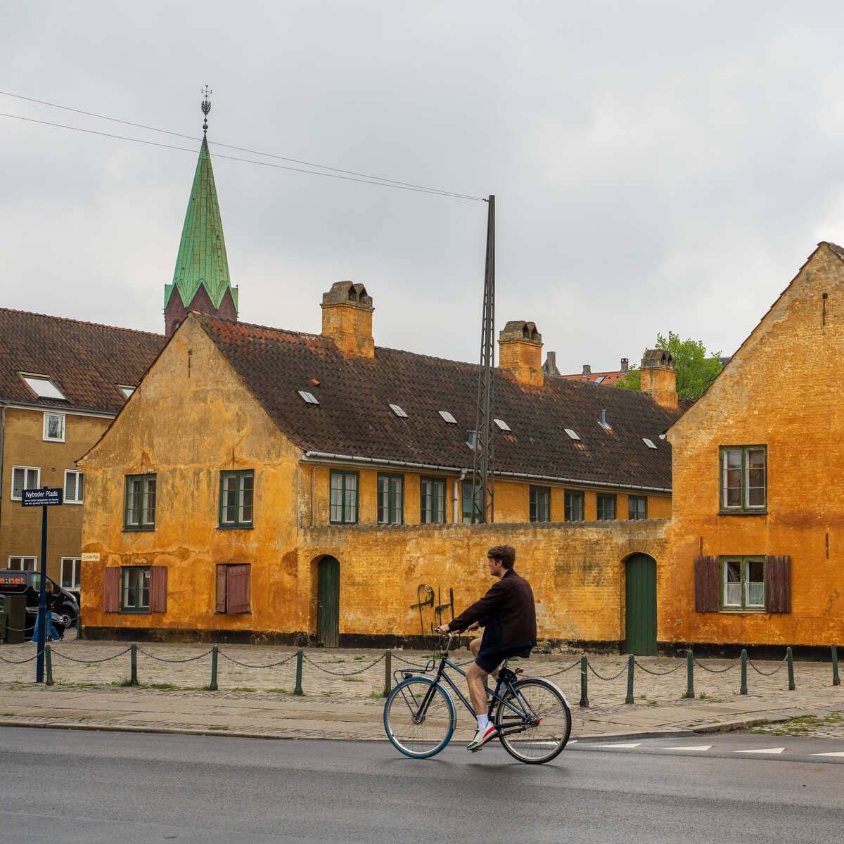 A Male Tourist Biking Across A Historic Zone In Copenhagen With Ocher-Colored Houses, Denmark, Scandinavia