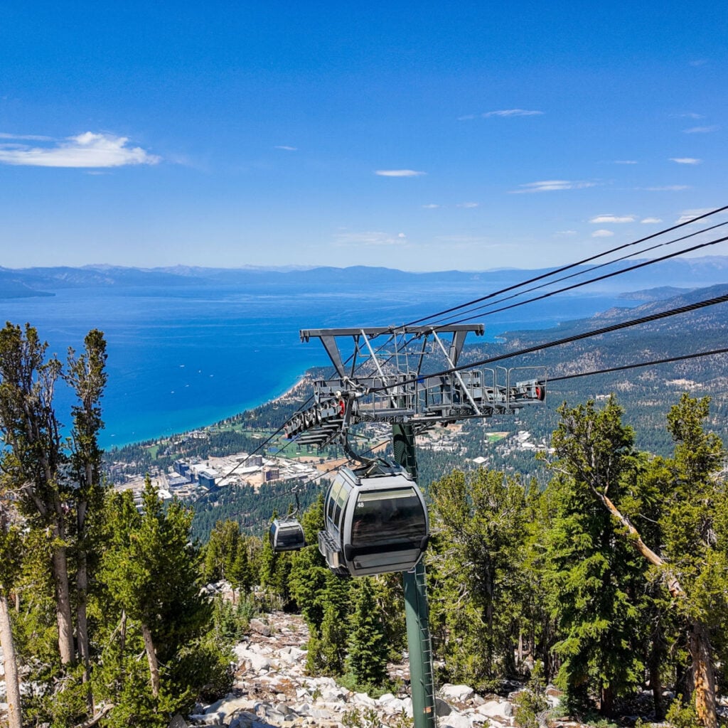A Ride on the Lake Tahoe Gondola Ski Lift looking at the the cable system and cars with Lake Tahoe and the Mountain in the Background as people ride up and down the mountain.