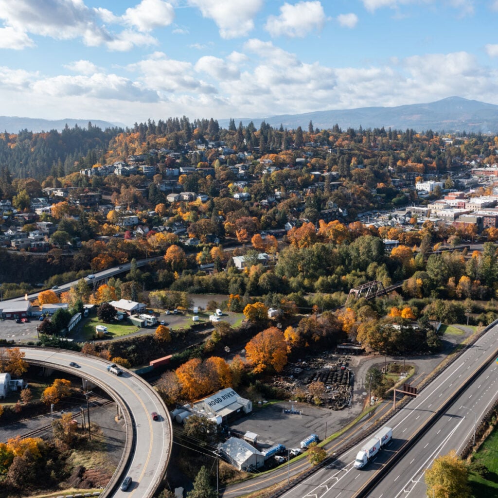 Aerial drone picture of Hood River, Oregon showing cityscape, I-84 freeway traffic, Chevron gas station, Fedex truck, Best Western, colorful trees in fall season
